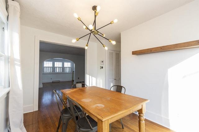 dining room with a chandelier, arched walkways, dark wood finished floors, and baseboards