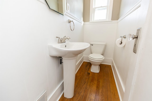 half bath with a sink, wood finished floors, toilet, and baseboards