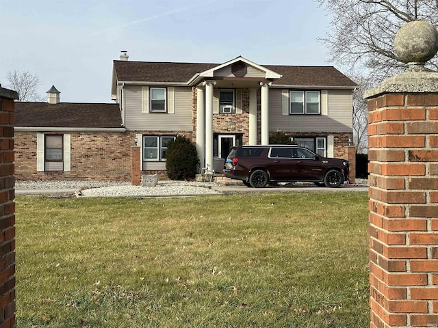 neoclassical home with brick siding, a front yard, and cooling unit