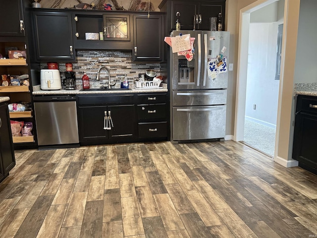 bar featuring wood finished floors, a sink, baseboards, appliances with stainless steel finishes, and backsplash