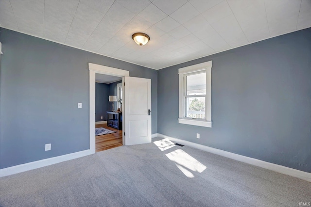 unfurnished room with carpet floors, visible vents, and baseboards