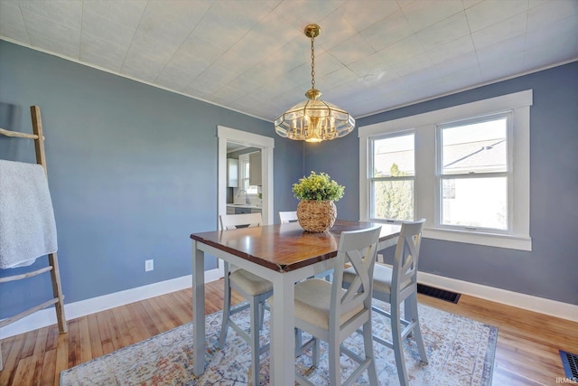 dining space with an inviting chandelier, light wood-type flooring, visible vents, and baseboards