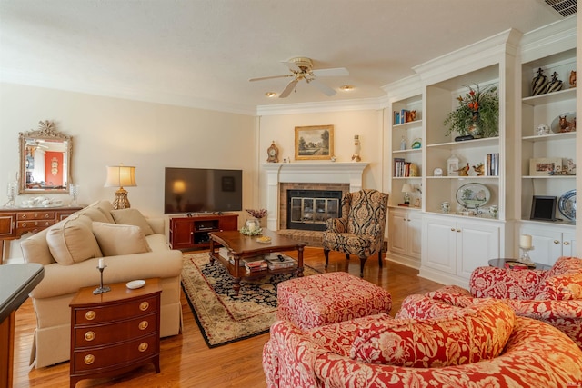 living area featuring visible vents, a ceiling fan, a glass covered fireplace, crown molding, and light wood-type flooring