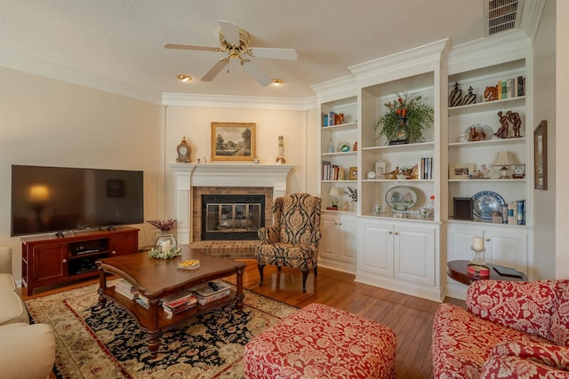 living area featuring crown molding, a fireplace, visible vents, a ceiling fan, and light wood-type flooring