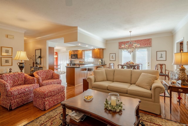 living area with ornamental molding, light wood-style flooring, and an inviting chandelier