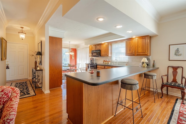 kitchen featuring pendant lighting, brown cabinets, crown molding, black microwave, and a peninsula