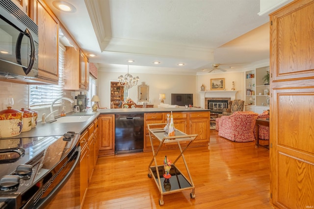 kitchen with a raised ceiling, a glass covered fireplace, ornamental molding, light wood-type flooring, and black appliances