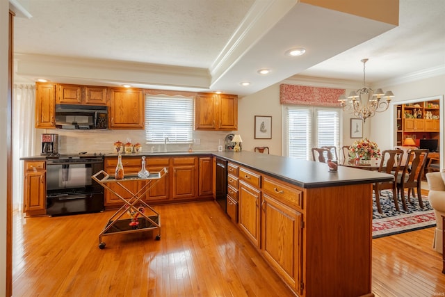 kitchen featuring a peninsula, a sink, black appliances, dark countertops, and decorative light fixtures