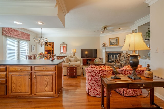 interior space featuring light wood-style floors, a glass covered fireplace, ornamental molding, and ceiling fan with notable chandelier