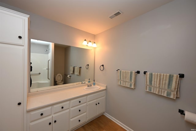 full bath with wood finished floors, vanity, visible vents, baseboards, and a shower