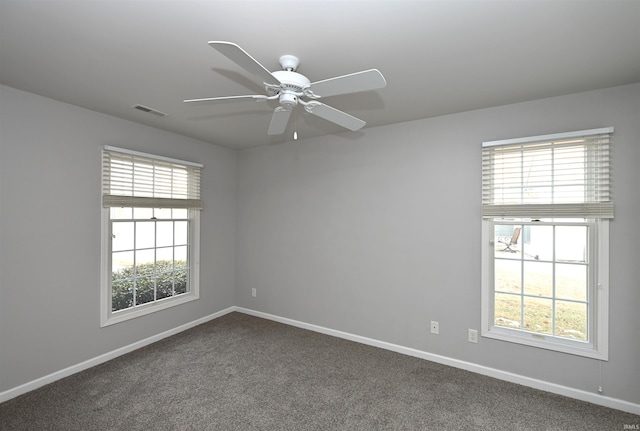 empty room featuring ceiling fan, dark carpet, visible vents, and baseboards