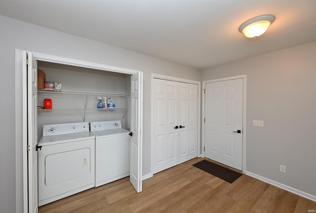 clothes washing area featuring light wood-type flooring, laundry area, washing machine and dryer, and baseboards