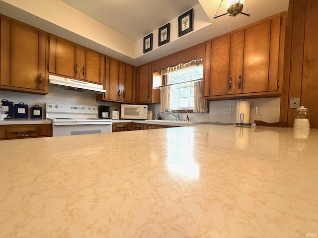 kitchen featuring under cabinet range hood, white appliances, a sink, light countertops, and brown cabinetry