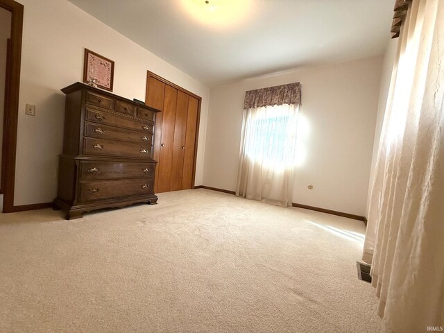 unfurnished bedroom with a closet, light colored carpet, and baseboards