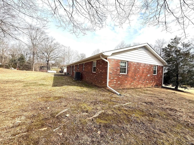 view of property exterior with brick siding, a lawn, and central AC unit