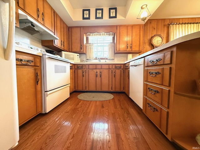 kitchen featuring white appliances, brown cabinetry, wood finished floors, light countertops, and under cabinet range hood