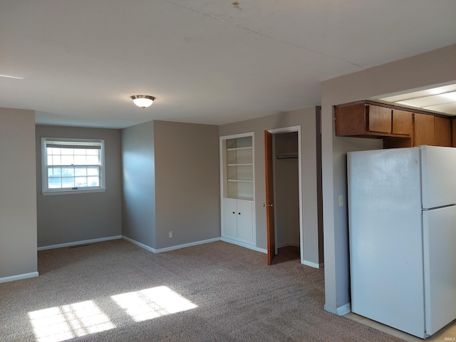 kitchen featuring baseboards, light colored carpet, freestanding refrigerator, and brown cabinets