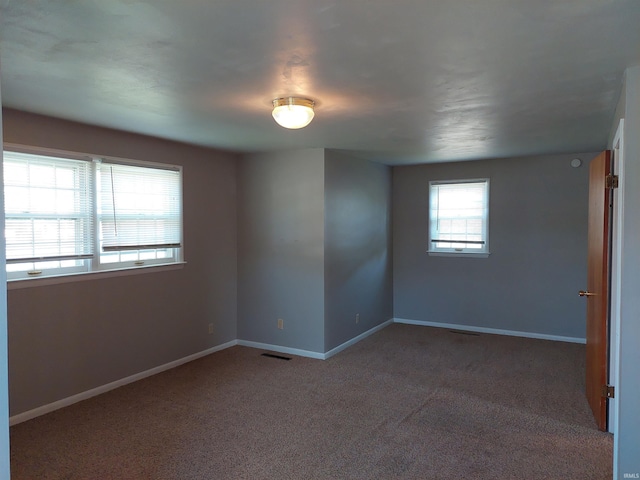 unfurnished room featuring dark colored carpet, visible vents, and baseboards