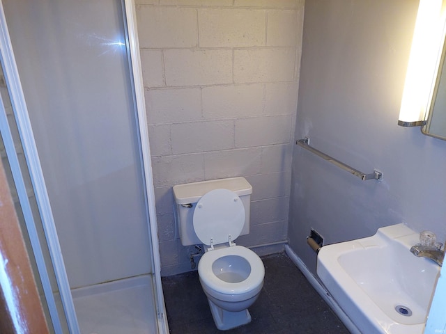 bathroom featuring a stall shower, a sink, toilet, and concrete block wall