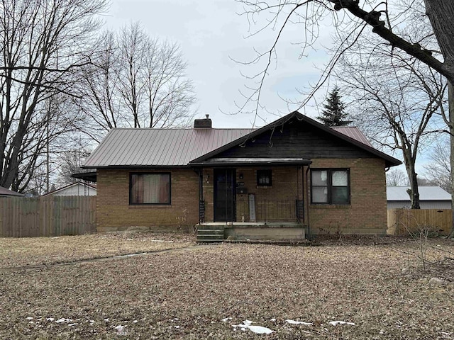 view of front of house with covered porch, brick siding, fence, and a chimney