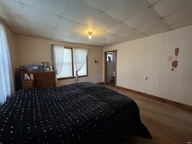 bedroom with a drop ceiling, wood finished floors, and baseboards