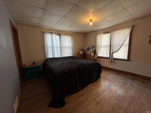 bedroom with wood finished floors, a paneled ceiling, and baseboards