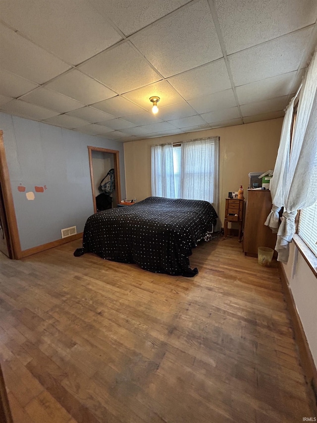 bedroom with a paneled ceiling, baseboards, visible vents, and wood finished floors