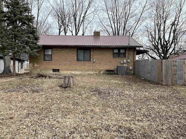 exterior space featuring brick siding, a chimney, central air condition unit, fence, and metal roof