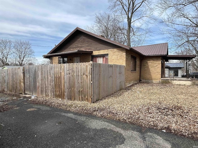 view of side of home with fence, metal roof, and brick siding