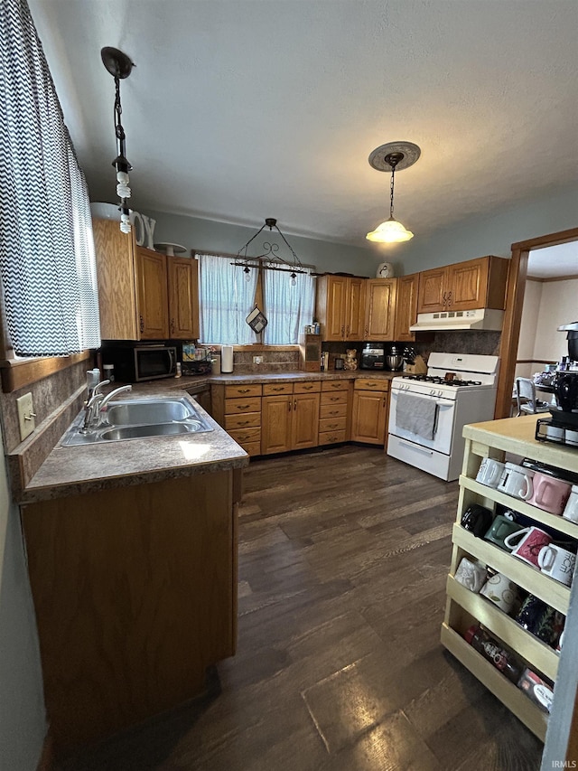 kitchen featuring pendant lighting, white gas range, a sink, and under cabinet range hood