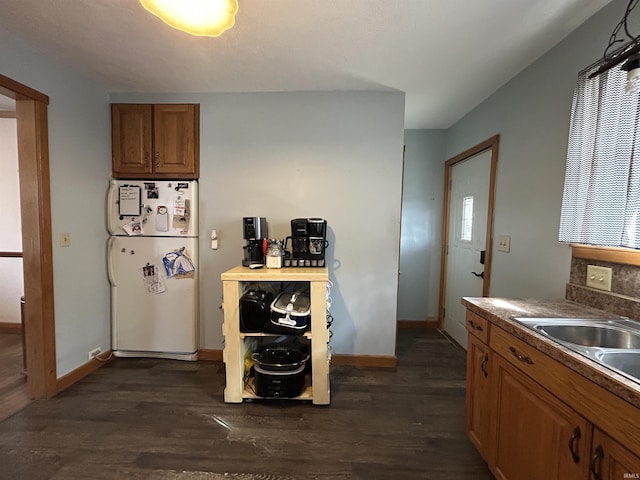 kitchen featuring dark wood-style floors, baseboards, brown cabinets, and freestanding refrigerator