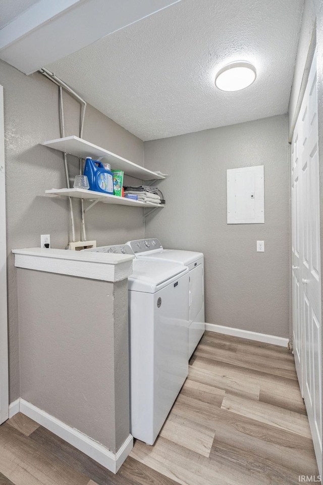 laundry room featuring electric panel, washer and clothes dryer, light wood-type flooring, baseboards, and laundry area