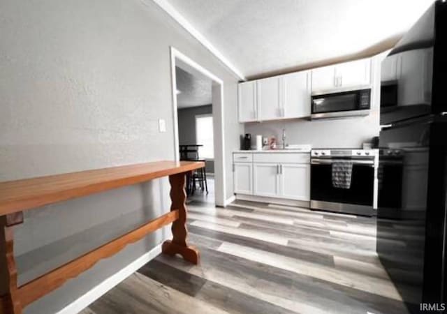 kitchen with stainless steel appliances, white cabinets, vaulted ceiling, light countertops, and light wood-type flooring