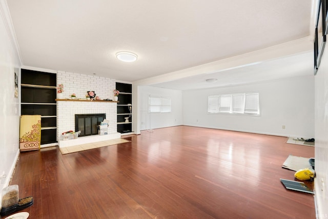 unfurnished living room featuring a brick fireplace, built in shelves, baseboards, and wood finished floors