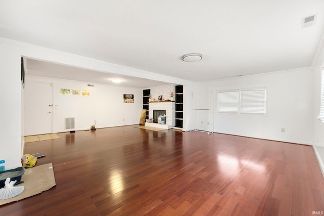 unfurnished living room with a brick fireplace, visible vents, crown molding, and wood finished floors