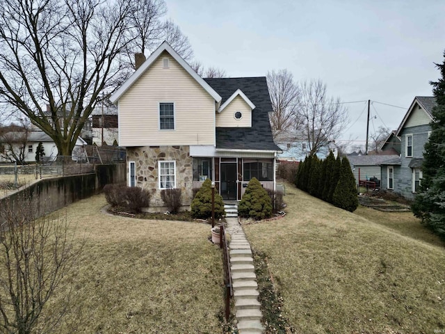 traditional home with stone siding, a front lawn, fence, and a sunroom