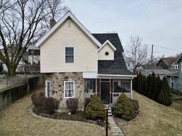 view of front of home with stone siding, a front yard, a sunroom, and fence