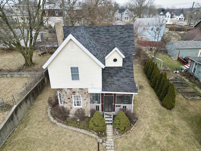 view of front of house featuring a fenced backyard, a shingled roof, a sunroom, stone siding, and a front yard