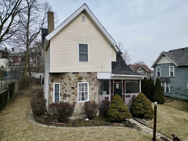 view of front facade with fence, a sunroom, stone siding, a front lawn, and a chimney