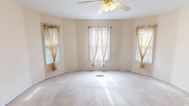 unfurnished room with a ceiling fan, light colored carpet, visible vents, and baseboards