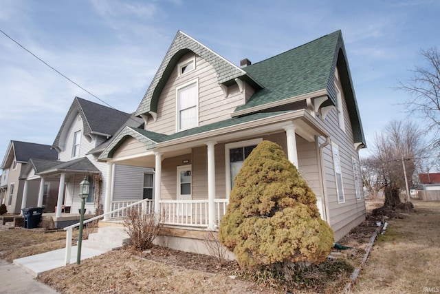 victorian home featuring covered porch, roof with shingles, and a chimney