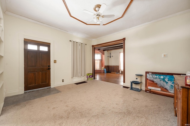 entrance foyer with ceiling fan, ornamental molding, dark colored carpet, and baseboards