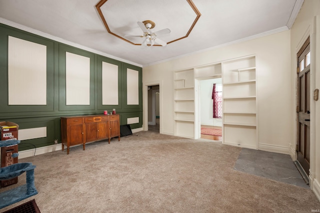 interior space with ceiling fan, crown molding, carpet flooring, built in shelves, and a decorative wall