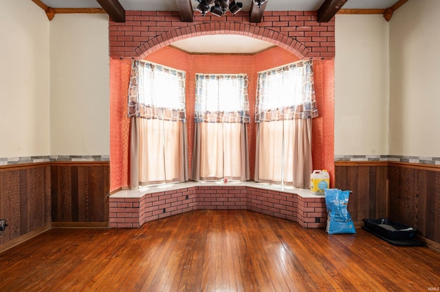 spare room with arched walkways, wainscoting, wood finished floors, and beam ceiling