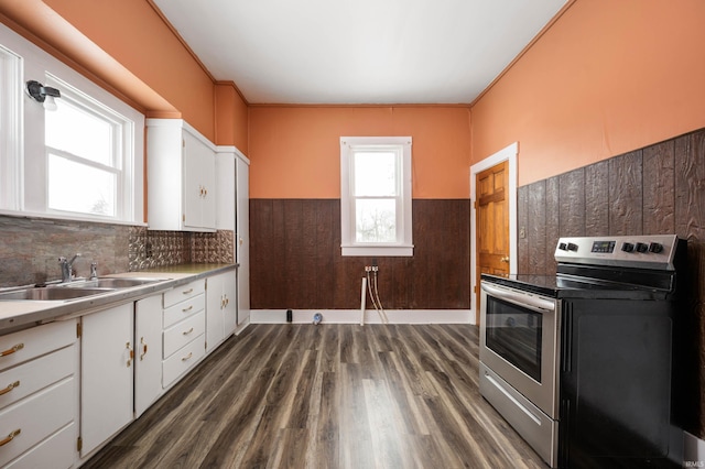 kitchen with electric range, white cabinets, wainscoting, light countertops, and a sink