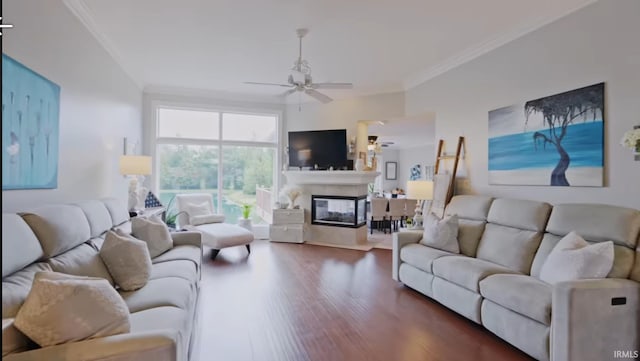 living room with ornamental molding, dark wood finished floors, a ceiling fan, and a multi sided fireplace