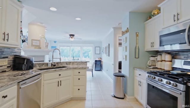 kitchen with appliances with stainless steel finishes, white cabinetry, a sink, and light stone countertops