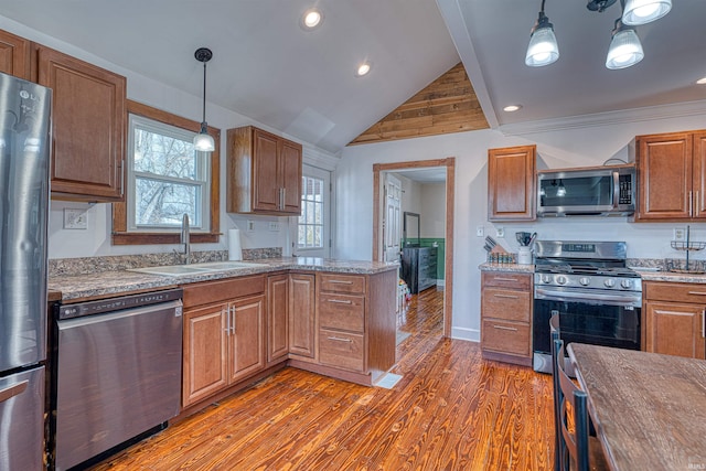 kitchen with stainless steel appliances, brown cabinetry, a sink, and decorative light fixtures