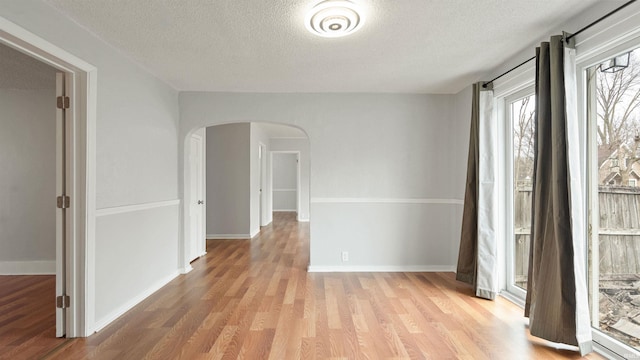 interior space with arched walkways, a textured ceiling, baseboards, and light wood-style floors