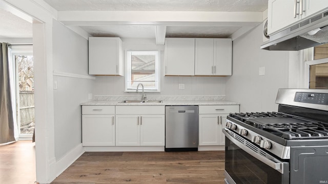 kitchen with beam ceiling, stainless steel appliances, light countertops, white cabinetry, and a sink